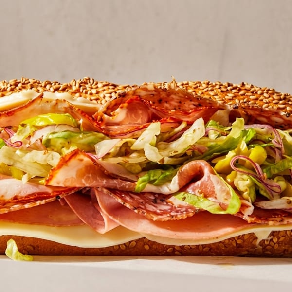 Large deli sub sandwich with various meats, cheese, lettuce, and peppers on a sesame seed bun.