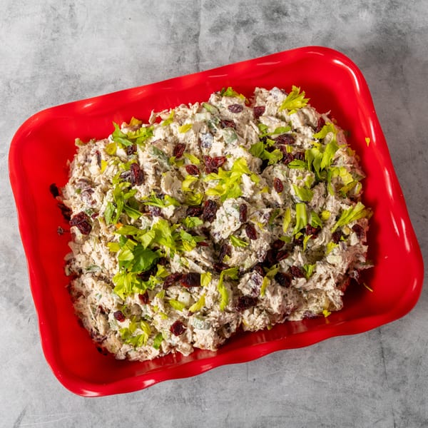 Chicken salad with cranberries and celery in a bright red serving dish on a gray surface.