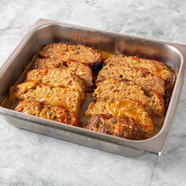Sliced meatloaf with gravy and red peppers in a metal serving pan.