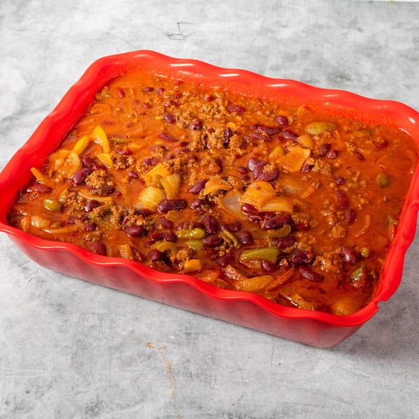 Hearty chili with ground beef, kidney beans, onions, and peppers in a red baking dish.