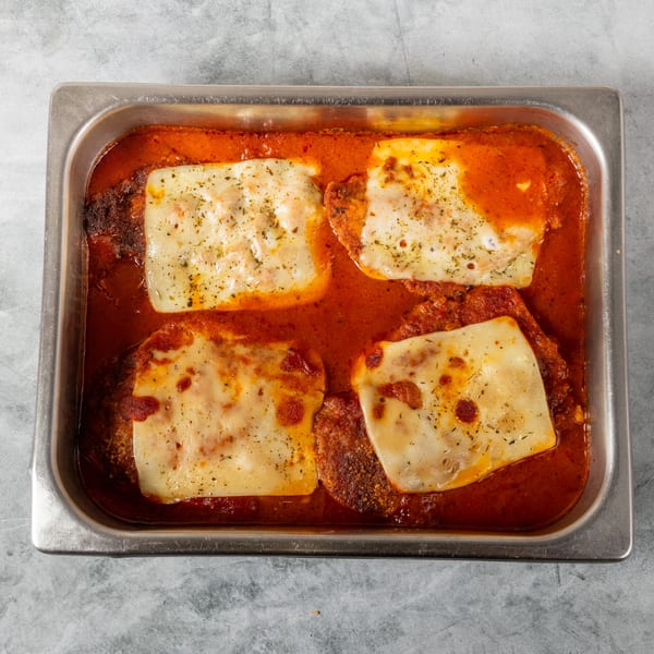 Four chicken parmesan cutlets with melted cheese and tomato sauce in a metal pan.