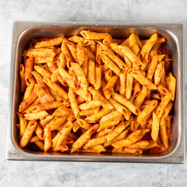 A large metal tray filled with penne pasta coated in a rich red tomato sauce.