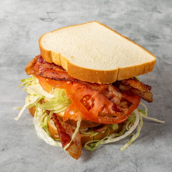 Bacon club sandwich stacked with crispy bacon, tomato, and shredded lettuce on white bread.