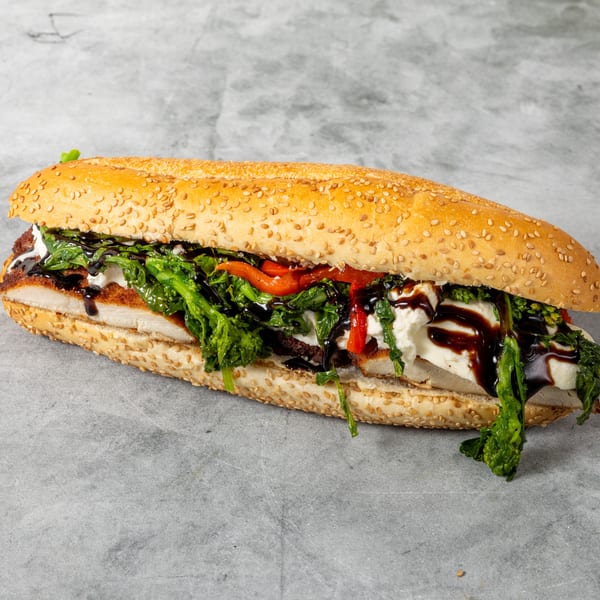 A long sesame seed hero sandwich filled with chicken cutlet, broccoli rabe, roasted peppers, and fresh mozzarella, drizzled with balsamic glaze.