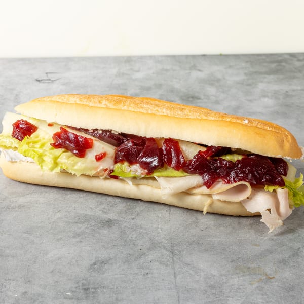 A turkey sub sandwich with lettuce, cheese, and cranberry sauce on a long roll.