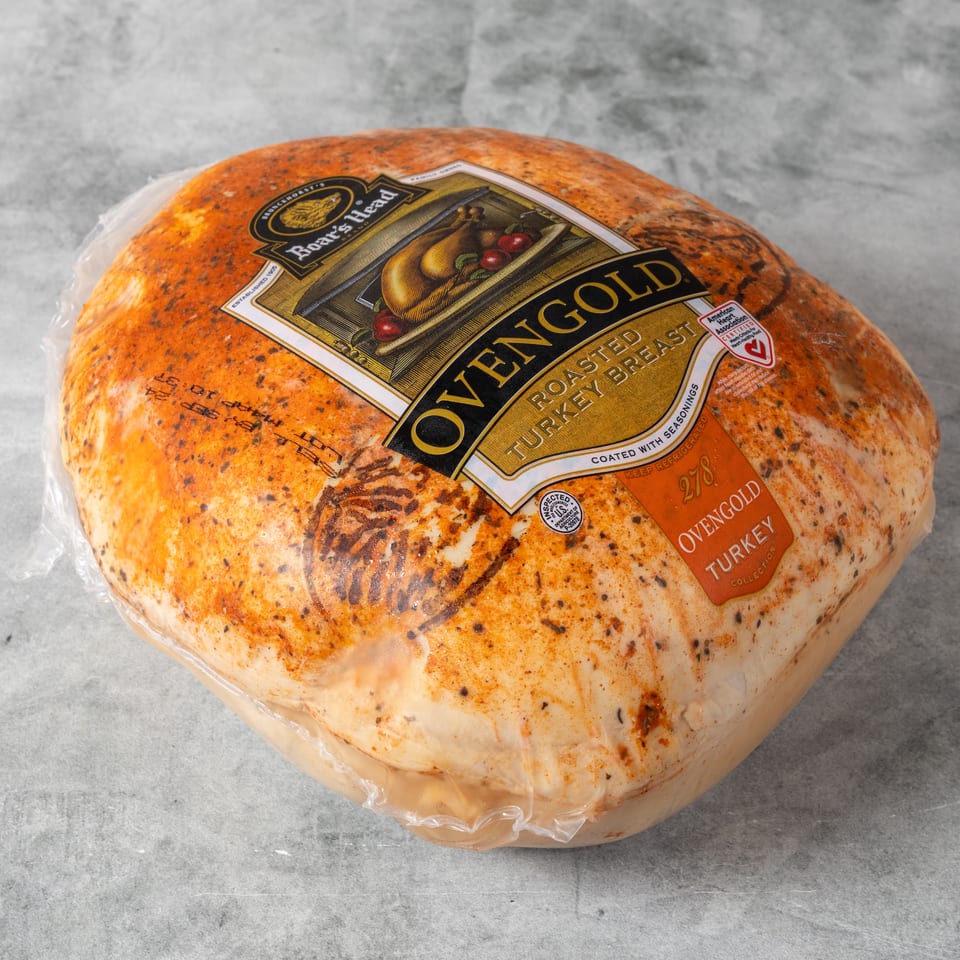 Seasoned Ovengold roasted turkey breast wrapped in plastic packaging on a gray surface.