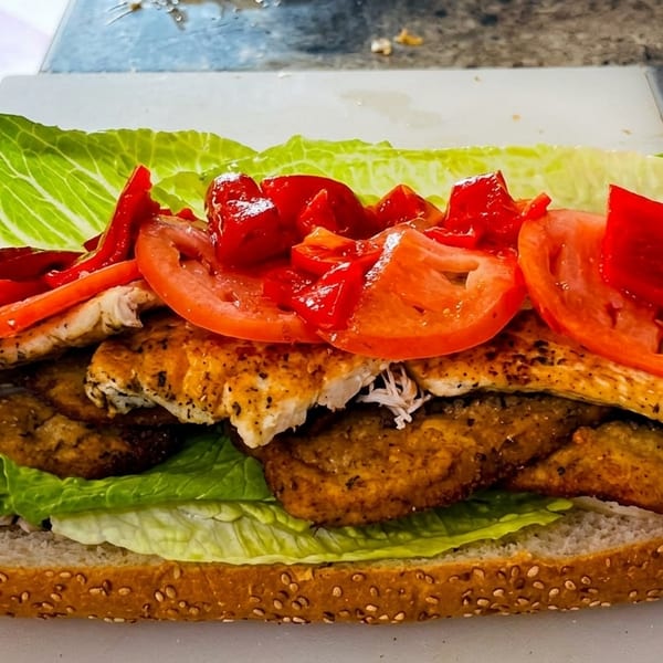 Loaded sub sandwich featuring grilled chicken, fried chicken, lettuce, tomatoes, and red peppers.