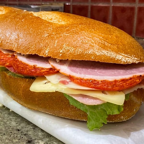 A large sub sandwich filled with ham, pepperoni, cheese, and lettuce on a crusty roll.