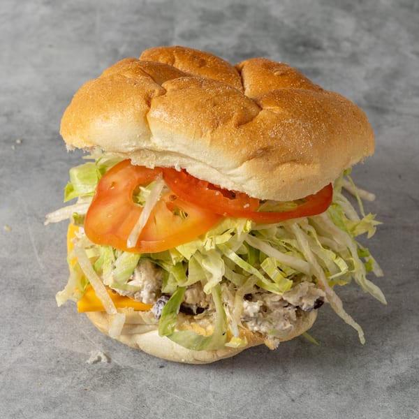 Loaded sandwich on a soft roll with sliced tomatoes, shredded lettuce, cheese, and creamy chicken salad filling.